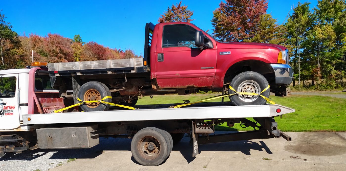 A red pickup truck loaded and strapped on the flatbed tow truck